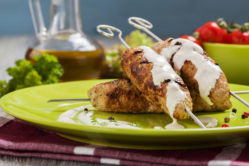 Barbecued kofta - kebeb topped with sauce with vegetables on a p