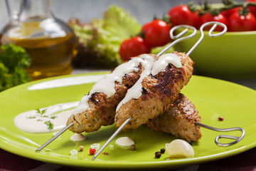 Barbecued kofta - kebeb topped with sauce with vegetables on a p