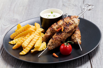 Barbecued kofta - kebeb with fries and vegetables on a plate.