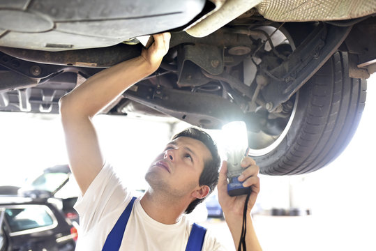 Mechanic examining underbody of a car in a garage