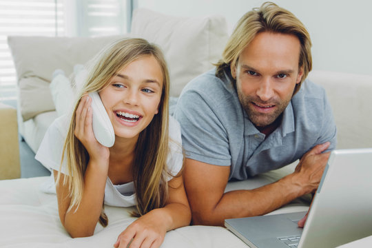Father and daughter lying on couch using laptop and telephone