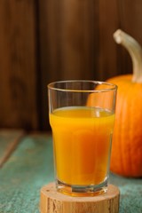 Glass of sweet pumpkin juice and whole pumpkin on wooden turquoi