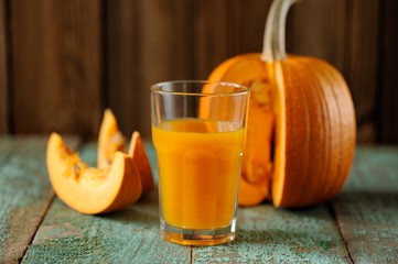 Glass of sweet pumpkin juice and cut pumpkin pieces on wooden tu