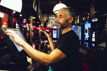 Waiter holding tray with beverages in an Irish pub while operating at till