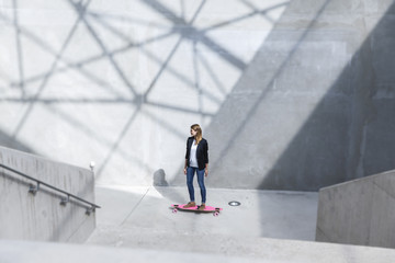 Businesswoman with pink skateboard in modern architecture