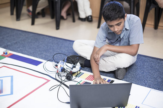 Schoolboy with laptop in robotics class testing vehicle on test track