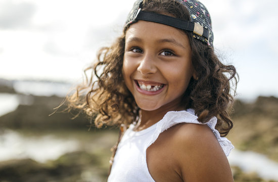 Spain, Gijon, portrait of smiling little girl with tooth gap at rocky coast