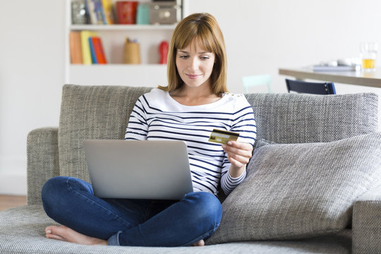 Thirty year old woman shopping using laptop and credit card at home