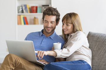 Happy successful young couple with laptop on sofa in modern apartment