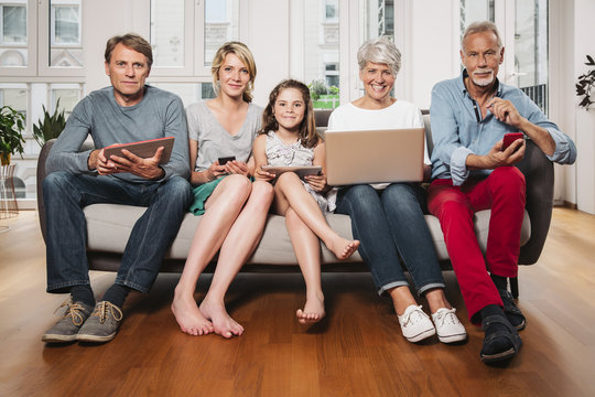 Group picture of three generations family with different digital devices sitting on one couch