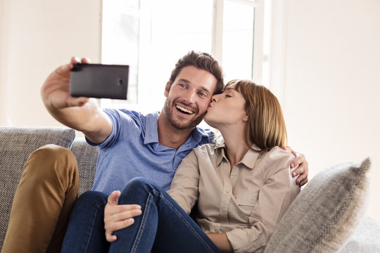 Cheerful lover couple taking a selfie with mobile phone. Kiss