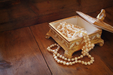 A beautiful antique golden jewelry box with natural white pearls on wooden table. retro filtered...