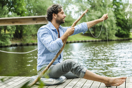 Man sitting on platform at the waterside with self-made fishing rod