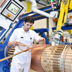 Arbeiter im Maschinenbau bedient Maschine zur Herstellung von Kupferspulen für Transformatoren // 
Workers operated machine for the production of copper coils for transformers - obrazy, fototapety, plakaty