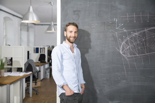 Smiling young man standing at blackboard in office