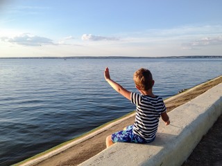 child sitting on embankment & waving at a boat