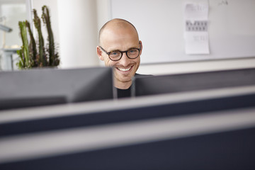 Smiling man in office behind computer screens