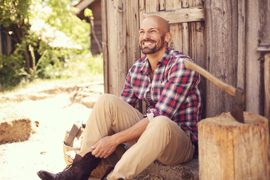 Portrait of grinning man wearing checked shirt putting on his boot