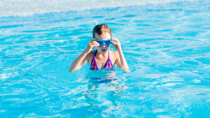 happy girl in blue goggles swimming and snorkeling in the swimming pool