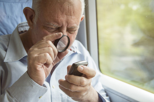 Senior man reading text on a cell phone with a magnifying glass