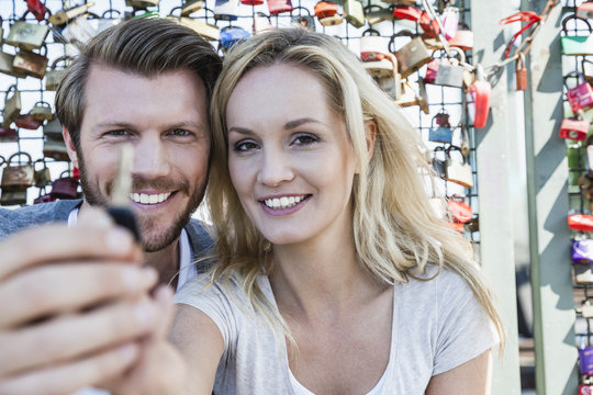 Germany, Cologne, portrait of smiling young couple holding key of love lock