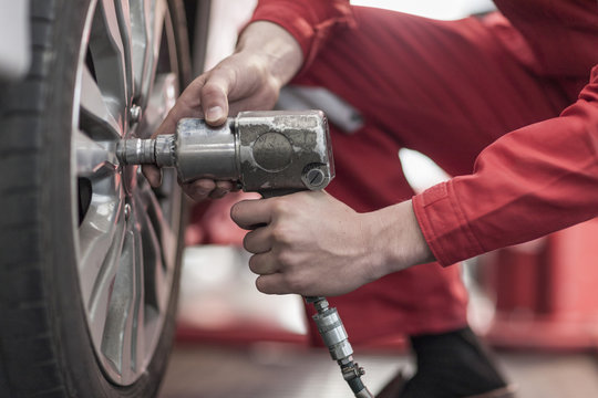 Car mechanic at work in repair garage, changing tires, impact driver