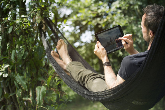 Relaxed man lying in hammock with digital tablet
