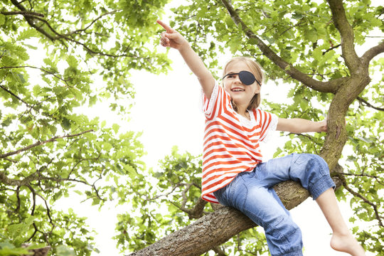 Girl dressed up as pirate sitting on a tree pointing finger