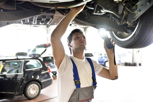 Mechanic examining underbody of a car in a garage