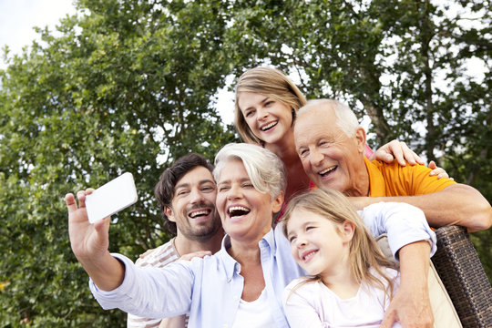 Happy extended family taking cell phone picture outdoors