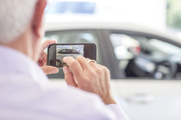Senior man taking picture of a new car in showroom