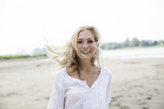Portrait of smiling blond woman with blowing hat on a beach