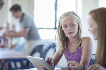 Two schoolgirls in classroom with digital tablet talking
