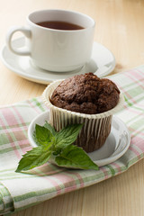 Chocolate muffin on white dish with sprig of mint linen napkin and a cup of tea