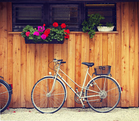 Fototapeta na wymiar Bicycle parked near a wooden cabin with geranium and herbs vases.