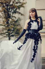 Fototapeta premium Beautiful young woman in white dress with black roses standing b