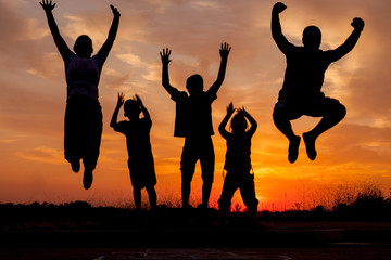 Young happy family jumping silhouettes  at sunset