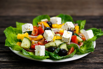Fresh Vegetable Greek Salad with Feta cheese, black olives, olives oil, cherry tomatoes, yellow pepper, red onion, cucumber. On wooden table.