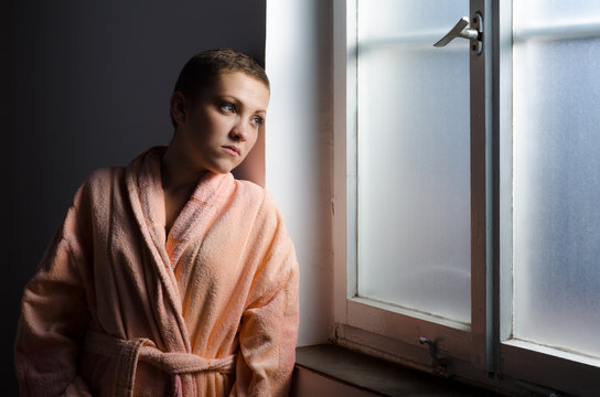 Young cancer patient standing in front of hospital window.
