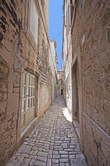 Fototapeta na wymiar Trogir, Croatia - Narrow cobbled street in Trogir center, antique Dalmatian city founded 4000 years ago.
