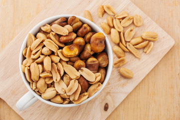 Peanut in a white bowl and spilling out of a bowl on wooden