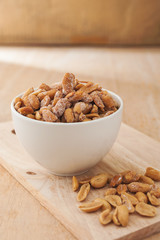 Peanut in a white bowl and spilling out of a bowl on wooden