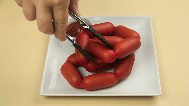 A string of Australian frankfurters called cheerios being lowered onto a plate with a bowl of ketchup.