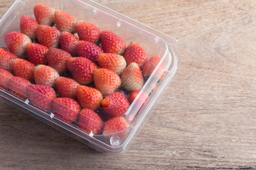 red ripe strawberry in plastic box of packaging on wood table