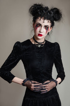 Young beautiful gothic woman with white skin and red lips with bloody drops wearing black collar with spikes. Red smokey eyes. Halloween makeup.