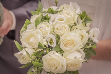 Wonderful white wedding flowers with many jewels and roses. The beautiful flowery accessory of the bride when she will marry her groom. Beautiful decoration. Gratulation in the background