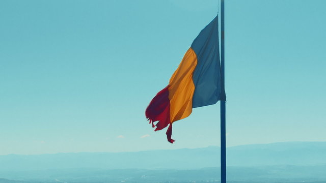 A frayed Romanian flag set against a light blue background of hazy mountains
