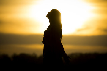 Twilight silhouette by beautiful sunny young woman in summer. The sun stands at the horizon and the girl becomes a very nice black silhouette