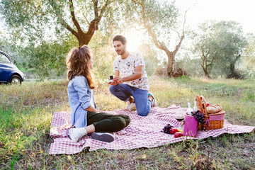 Young loving couple at a picnic in countryside of Tuscany, Italy. Marriage proposal of a young man...