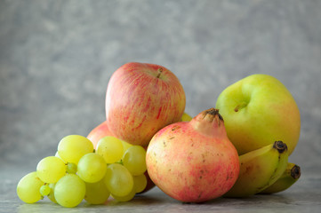 Frutta fresca di stagione, banane, mele, uva e melograno in primo piano sfondo marmo